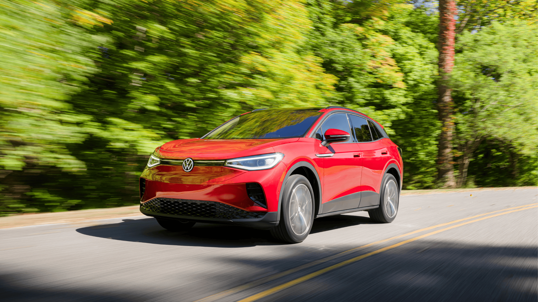 2023 Volkswagen ID.4 electric SUV in vibrant red driving along a scenic road surrounded by lush greenery, showcasing its modern design and eco-friendly appeal.