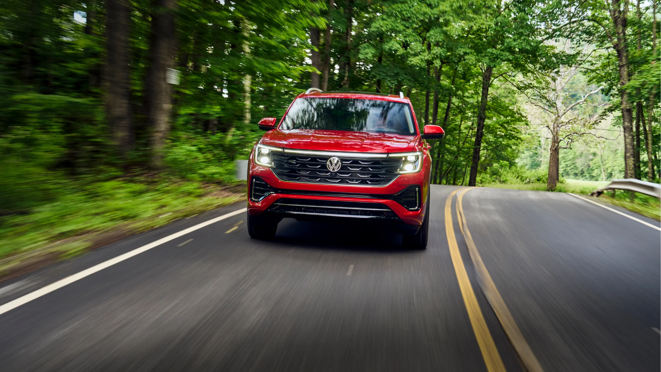 Front view of a red 2025 Volkswagen Atlas driving on a scenic forest road.