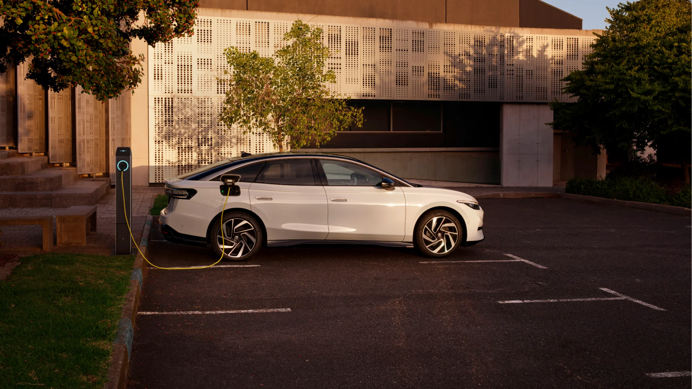 Side view of a white 2025 Volkswagen ID.7 charging at a station in daylight.