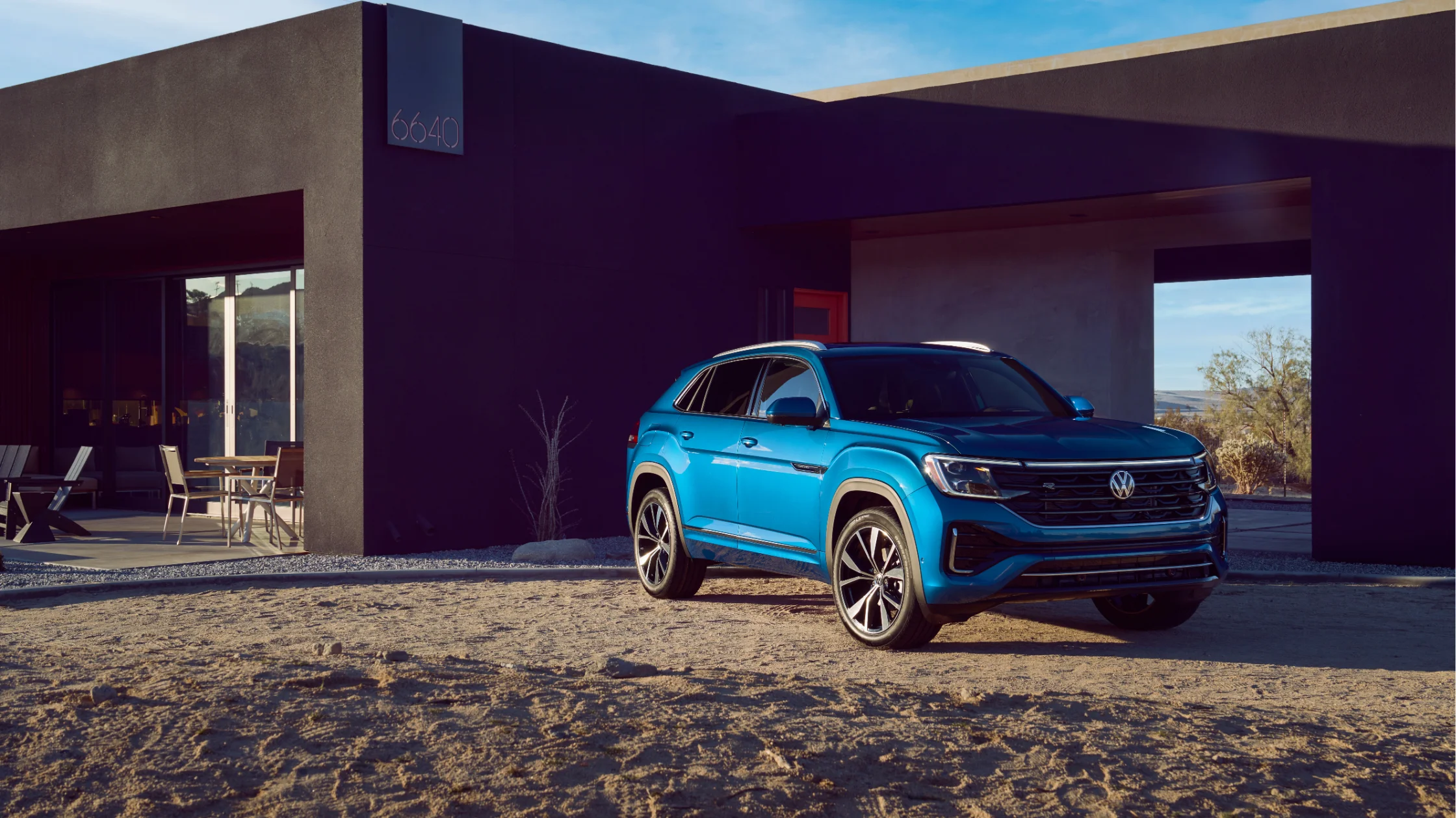 2025 Volkswagen Atlas Cross Sport in blue parked outside a modern home.