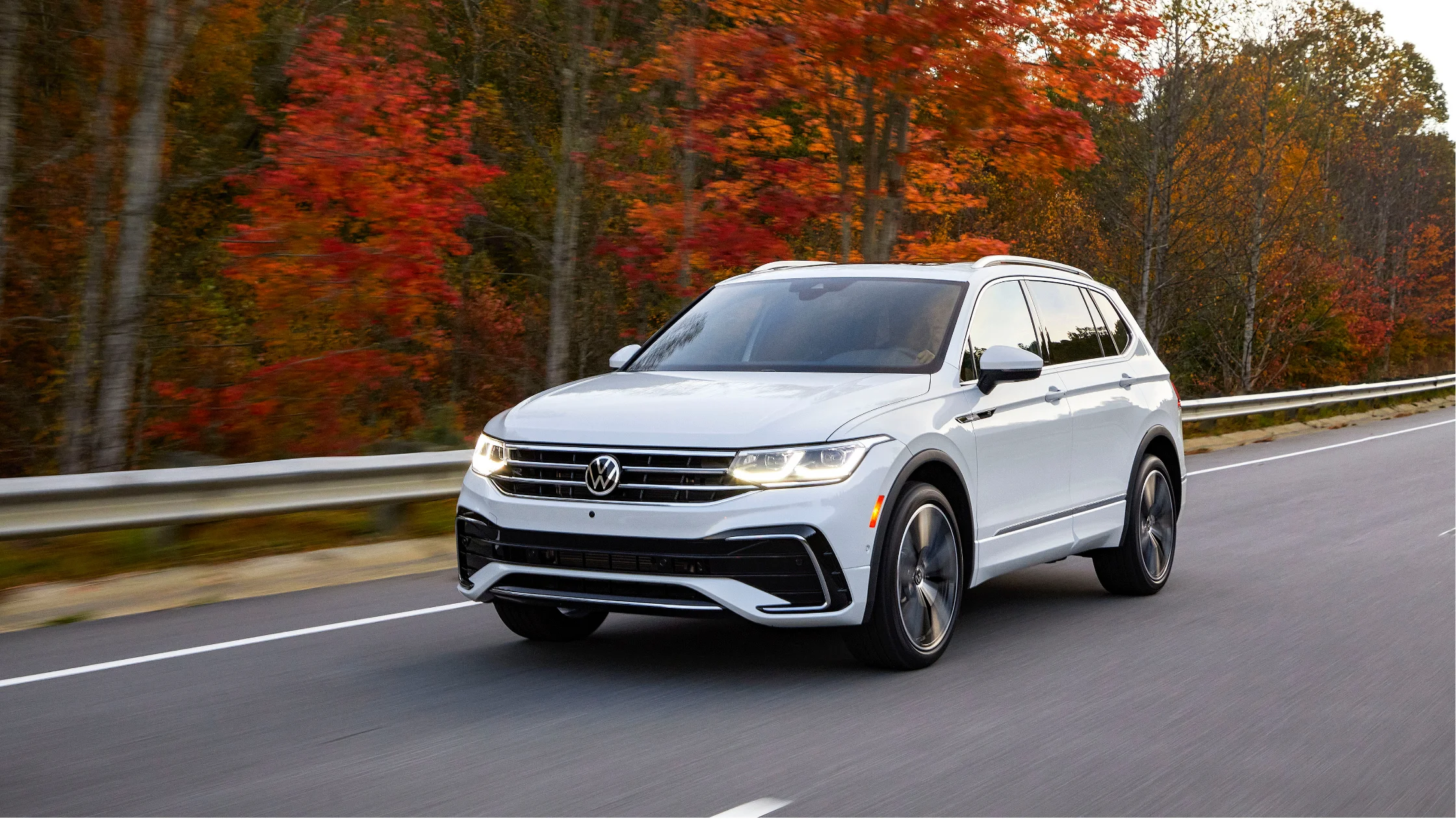2025 Volkswagen Tiguan driving on a road surrounded by vibrant autumn trees.