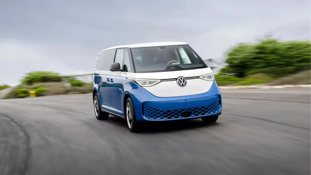 A blue and white 2025 Volkswagen ID. Buzz driving on a curvy road.