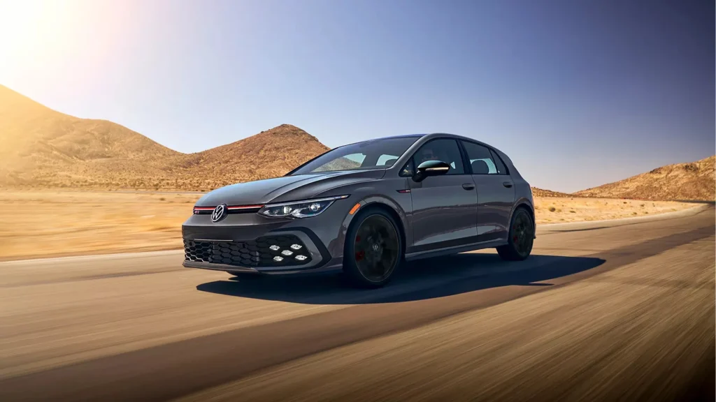 The 2025 Volkswagen Golf GTI hot hatch is seen in motion on a sunlit road surrounded by desert terrain.