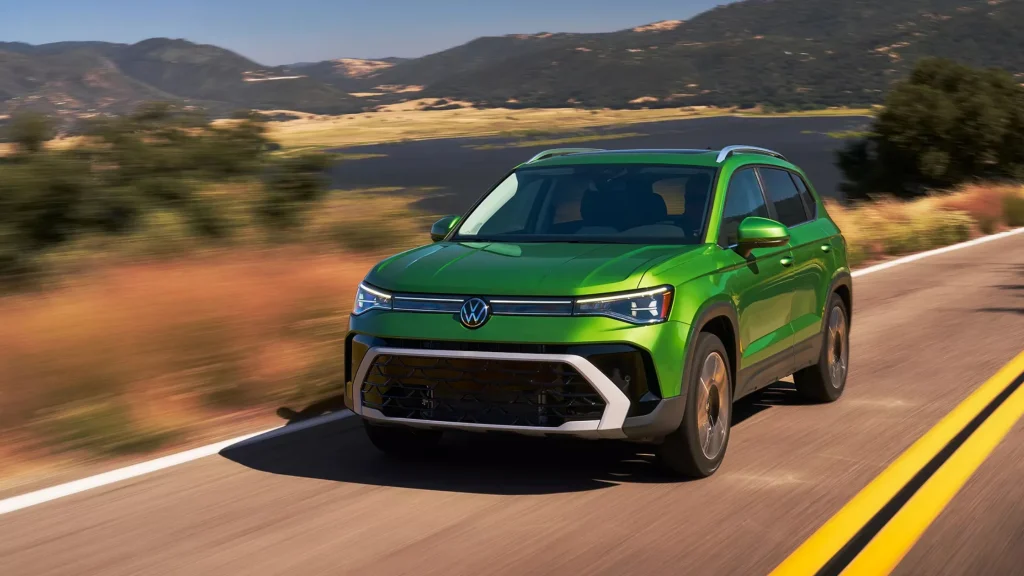 Green 2025 Volkswagen Taos cruising on a highway with hills and lake in the background.