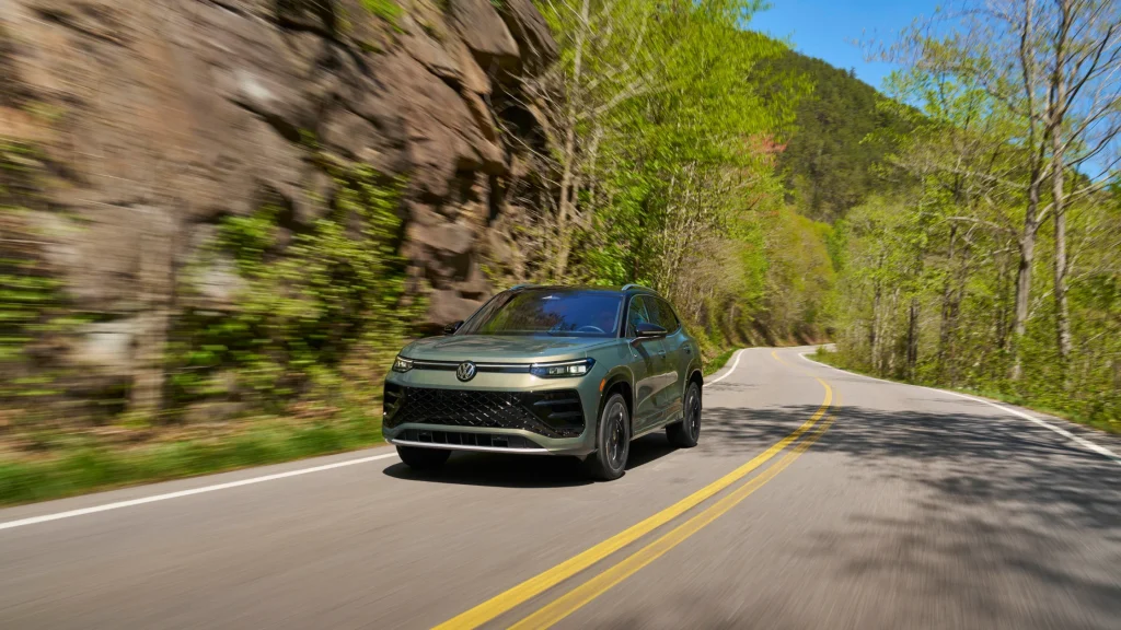 2026 Volkswagen Tiguan SEL R-Line Turbo in green driving on a curvy forest highway in daylight.
