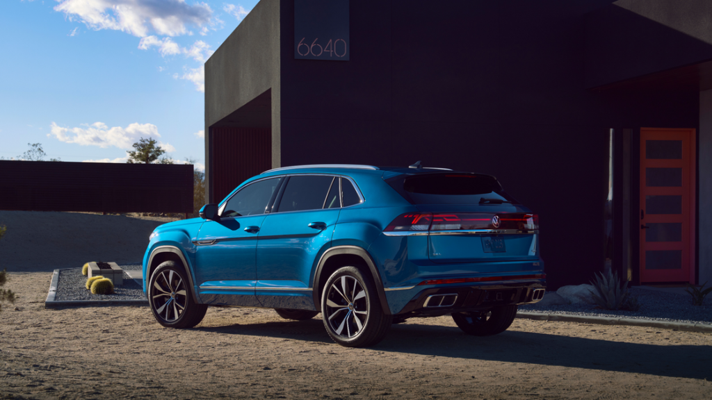 Rear three-quarter view of a blue 2025 Volkswagen Atlas Cross Sport parked beside a modern black home.
