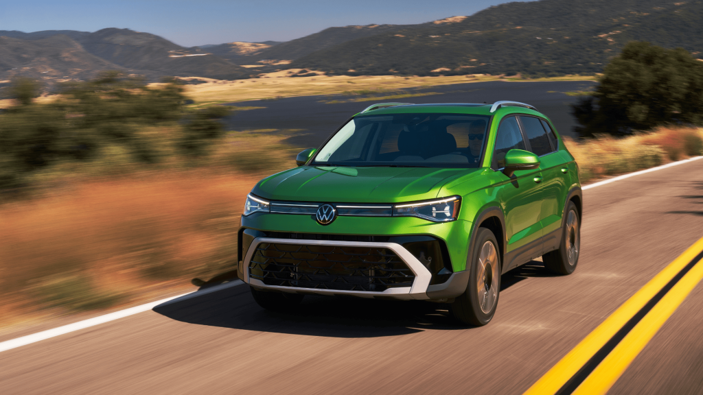 Green 2025 Volkswagen Taos SUV on a sunny highway near water and rolling hills.