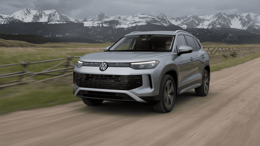Silver 2025 Volkswagen Tiguan SUV driving on a dirt road with snow-capped mountains in the background.