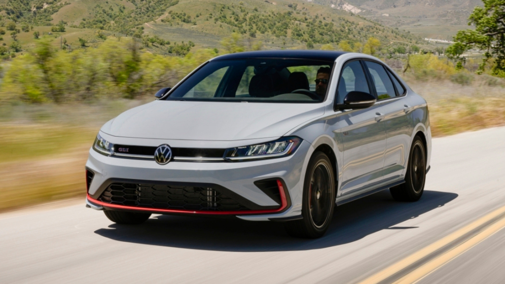 2025 Volkswagen Jetta GLI in white driving on a scenic road with sporty front grille design.