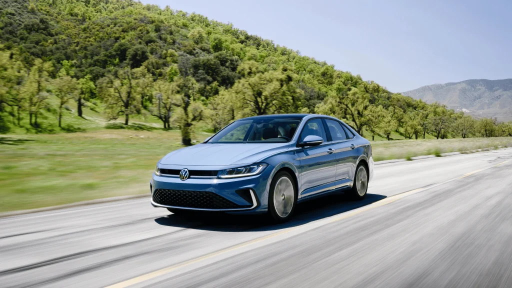 2026 Volkswagen Jetta sedan driving on a scenic open road with aerodynamic styling and LED headlights.