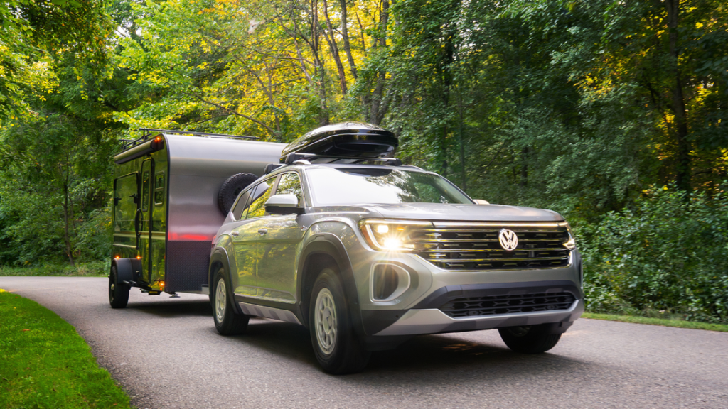 2025 Volkswagen Atlas towing a travel trailer on a forest road, showcasing capability and stability.