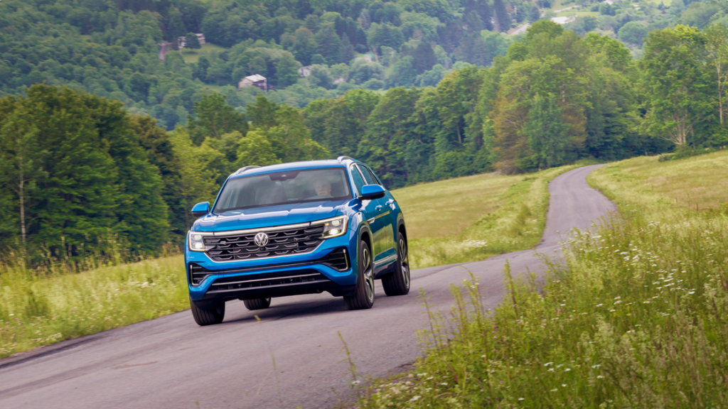 2025 Volkswagen Atlas Cross Sport driving through a winding countryside road with lush green hills.