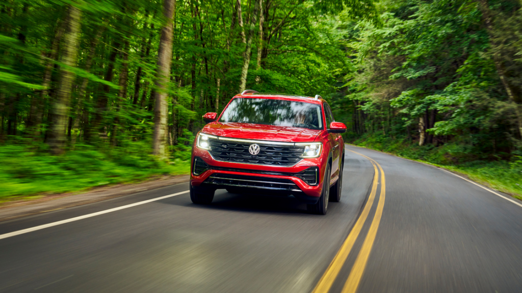 2026 Volkswagen Atlas SUV driving on forest road with red exterior showcasing front grille and stance.