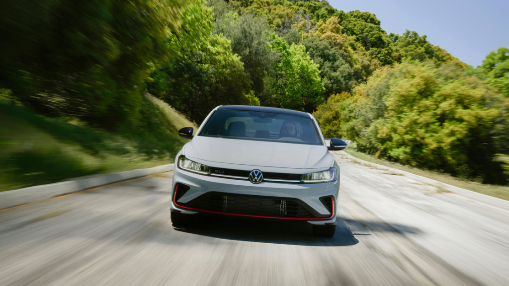 2026 Volkswagen Jetta GLI sport sedan driving toward camera on a curving road with motion blur.