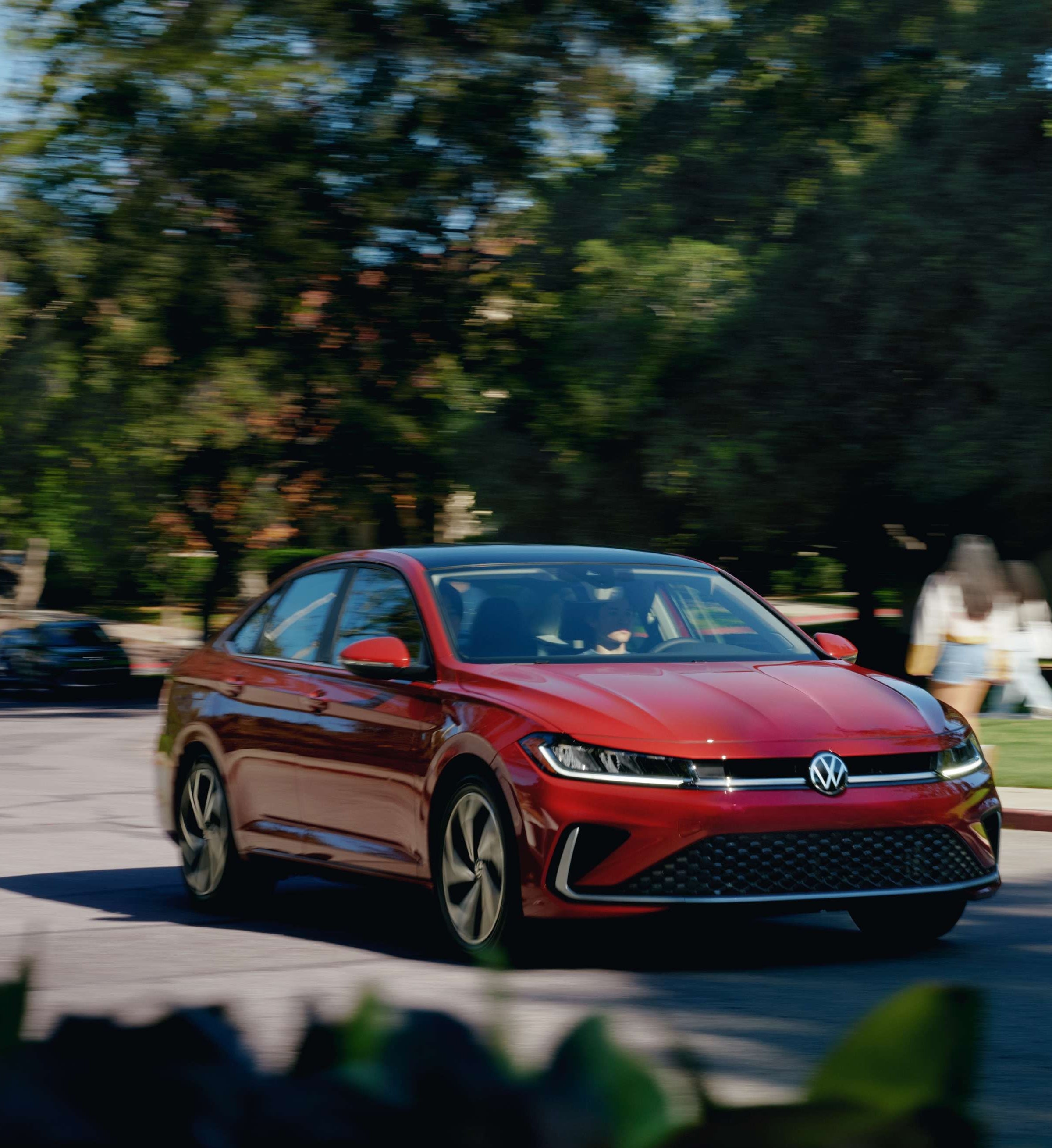 Red Volkswagen sedan driving on a tree-lined road