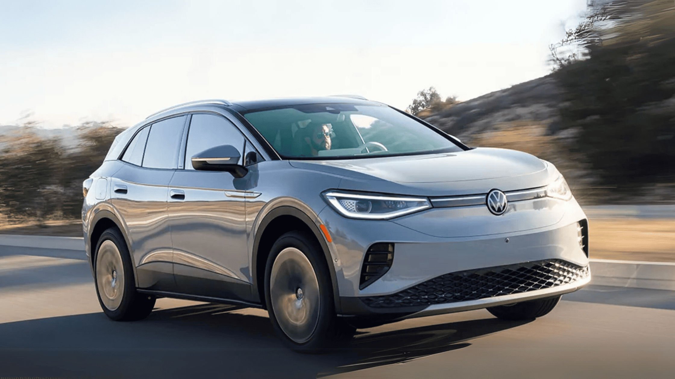 2023 Volkswagen ID.4 electric SUV in silver driving on a scenic road with blurred trees in the background, highlighting its sleek design, energy efficiency, and modern styling.