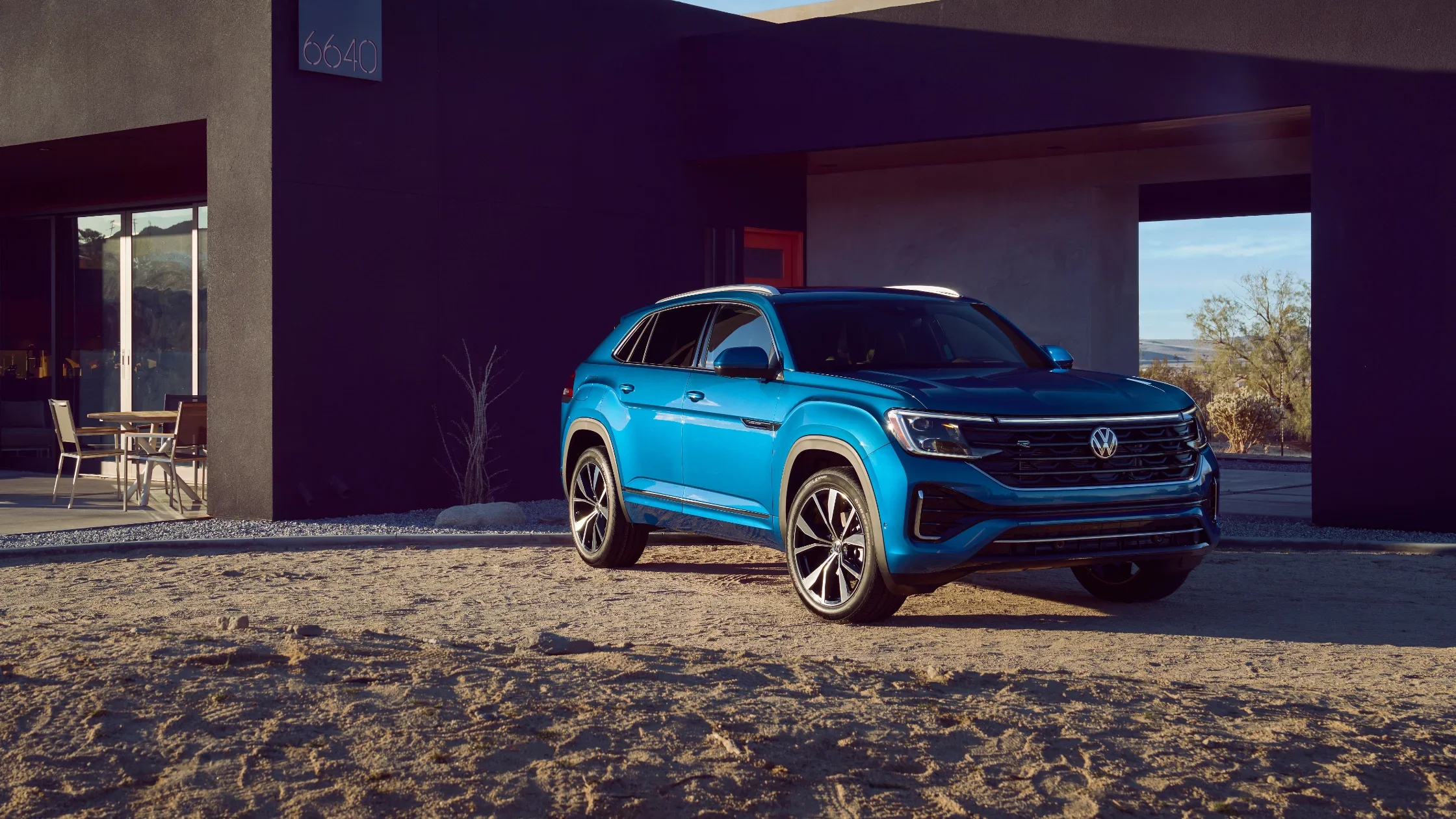 2024 Volkswagen Atlas Cross Sport in blue parked outside a modern home.