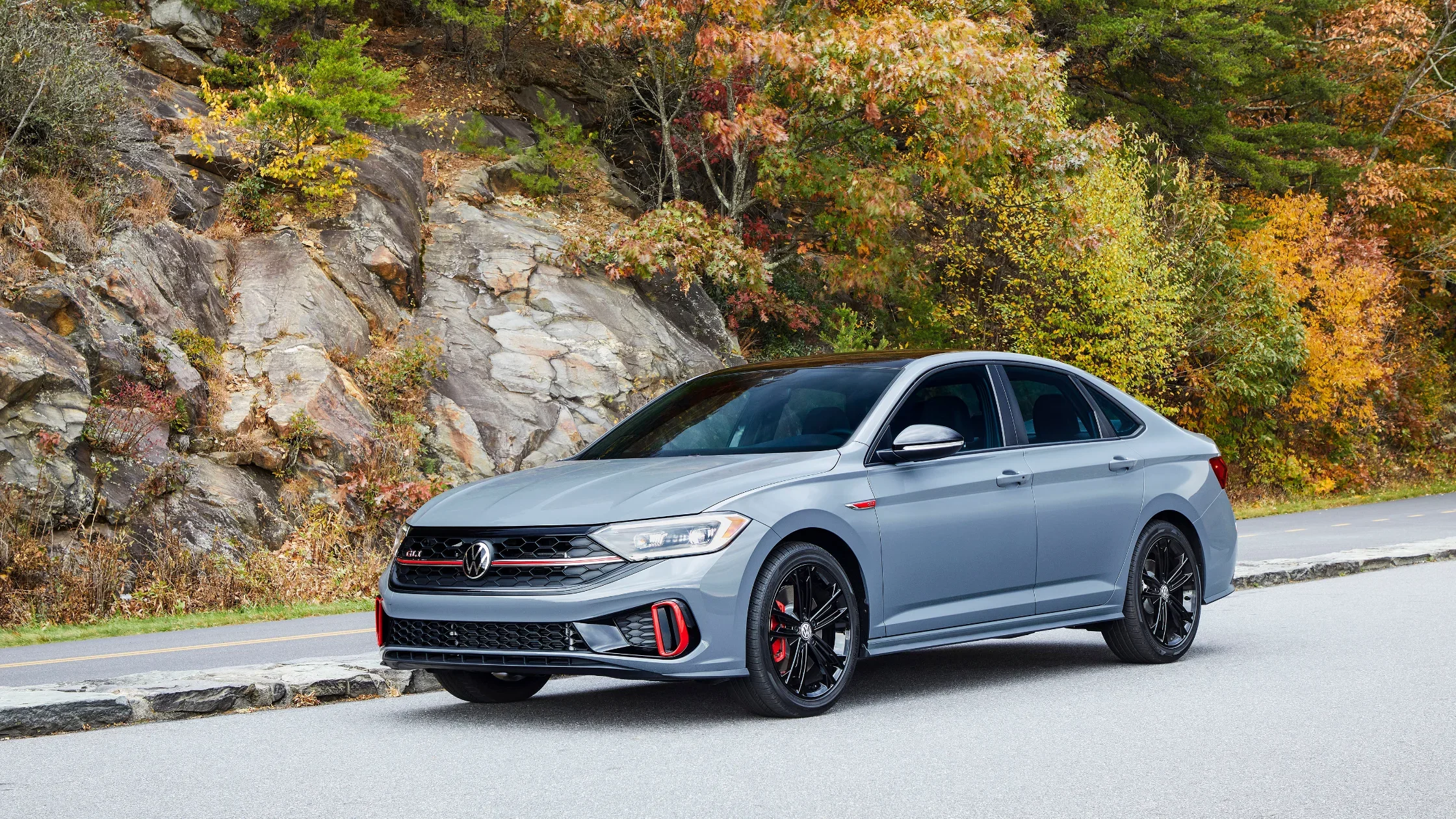 2024 Volkswagen Jetta GLI in grey parked on scenic road with autumn foliage.