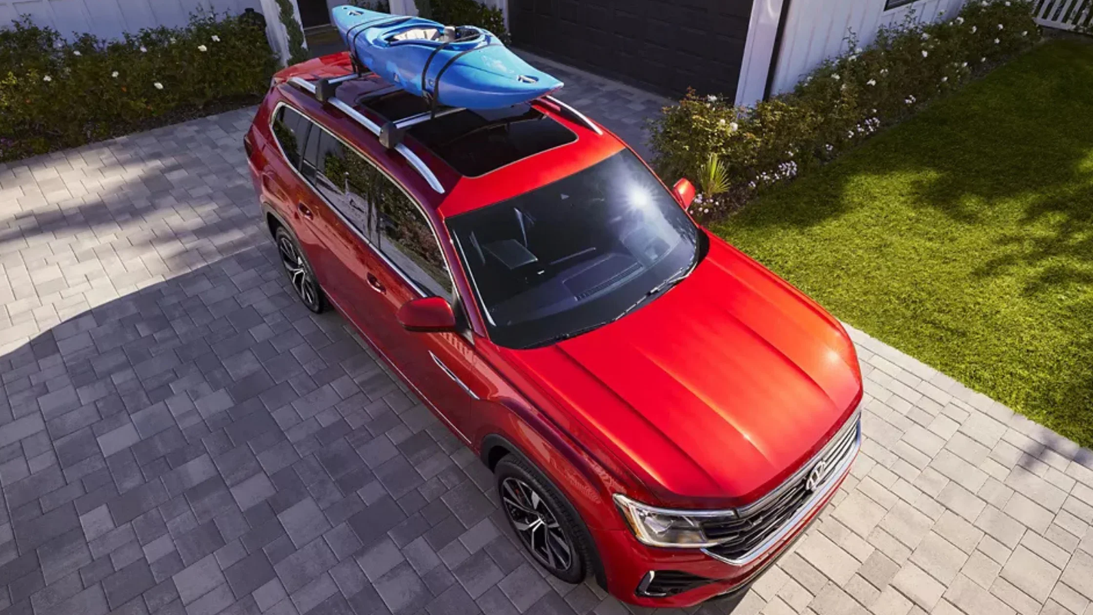 Top-down view of red 2025 Volkswagen Atlas with blue kayak on roof in driveway