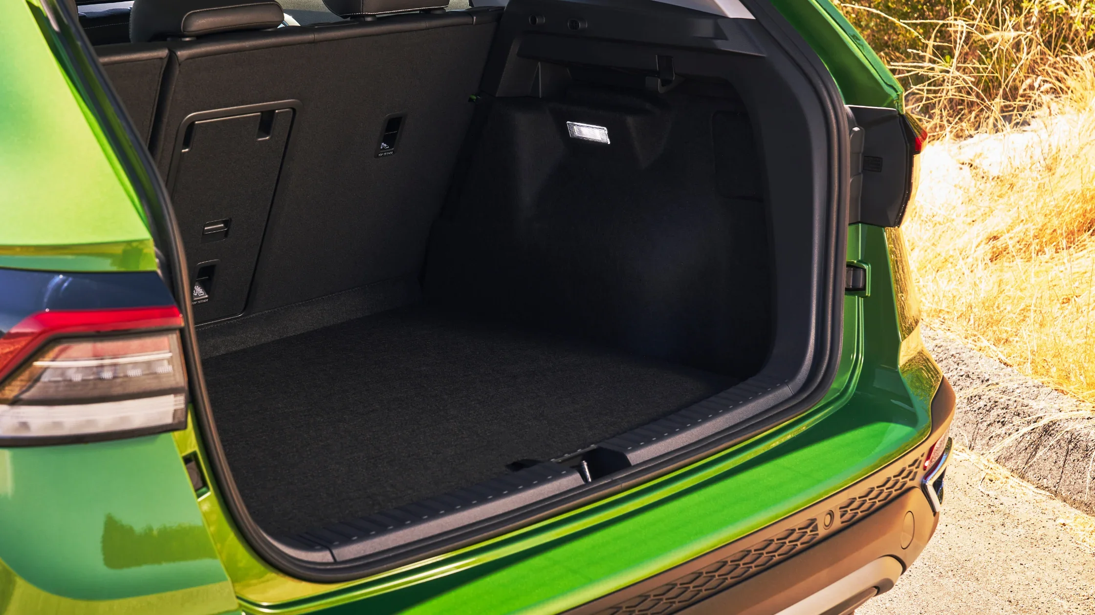 Open trunk space of the 2025 Volkswagen Taos in green with folded rear seats and cargo area light.