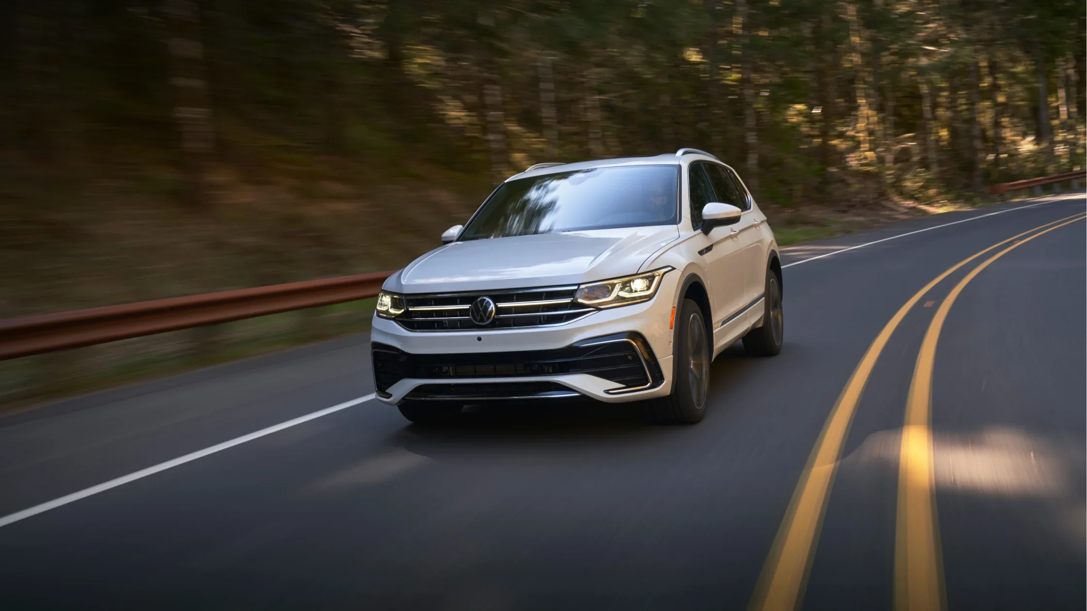 The 2025 Volkswagen Tiguan driving smoothly on a scenic forest road.