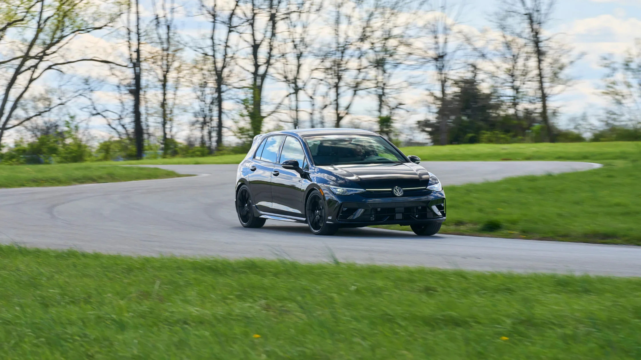 2025 Volkswagen Golf R in black taking a curve on a track with dynamic body stance.