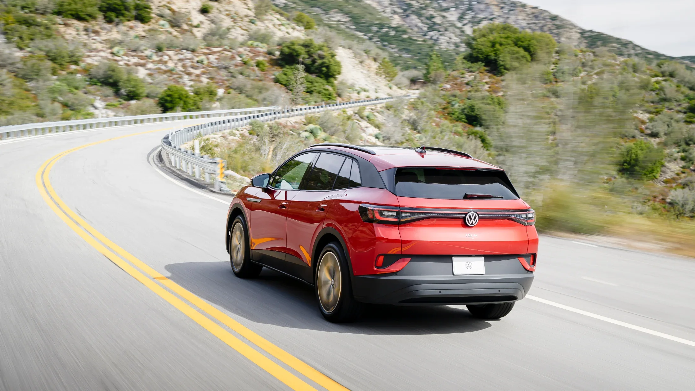 2025 Volkswagen ID.4 in red driving on a mountain road, showing LED taillights and rear design.