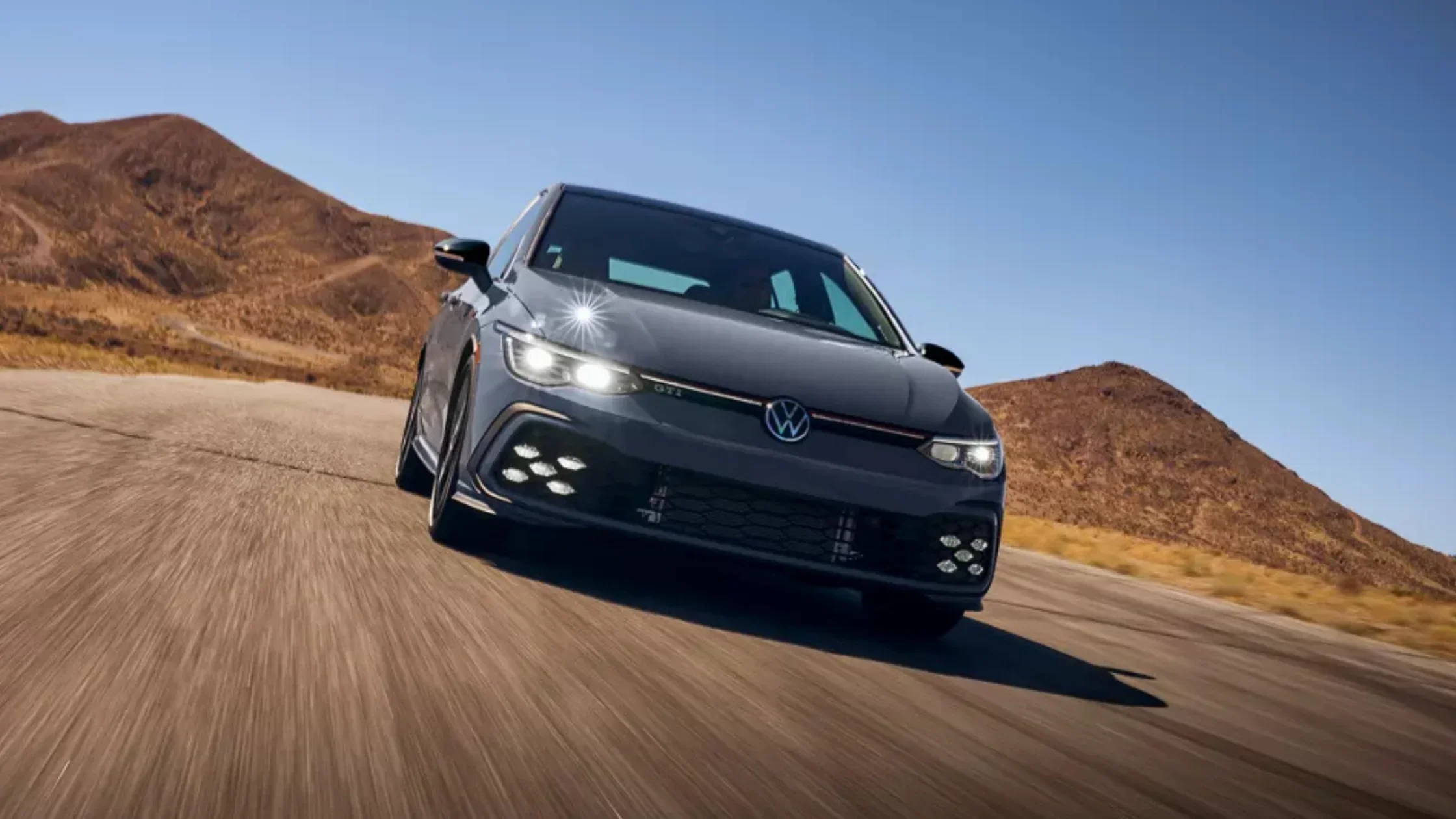 The 2025 Volkswagen Golf GTI speeding down a desert highway with a bold front grille.