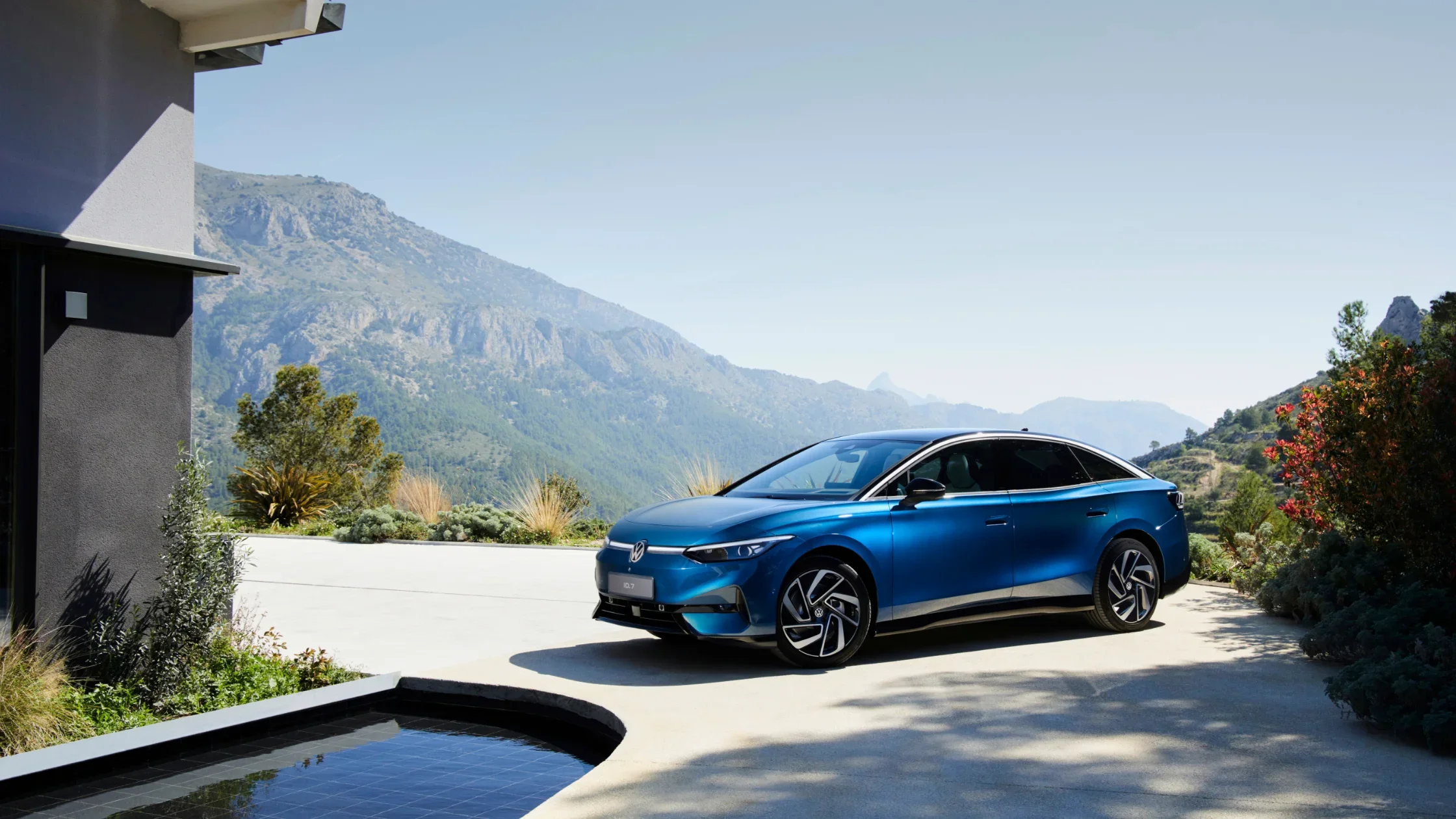 A sleek blue Volkswagen ID.7 positioned in a tranquil outdoor setting with lush greenery and hills.