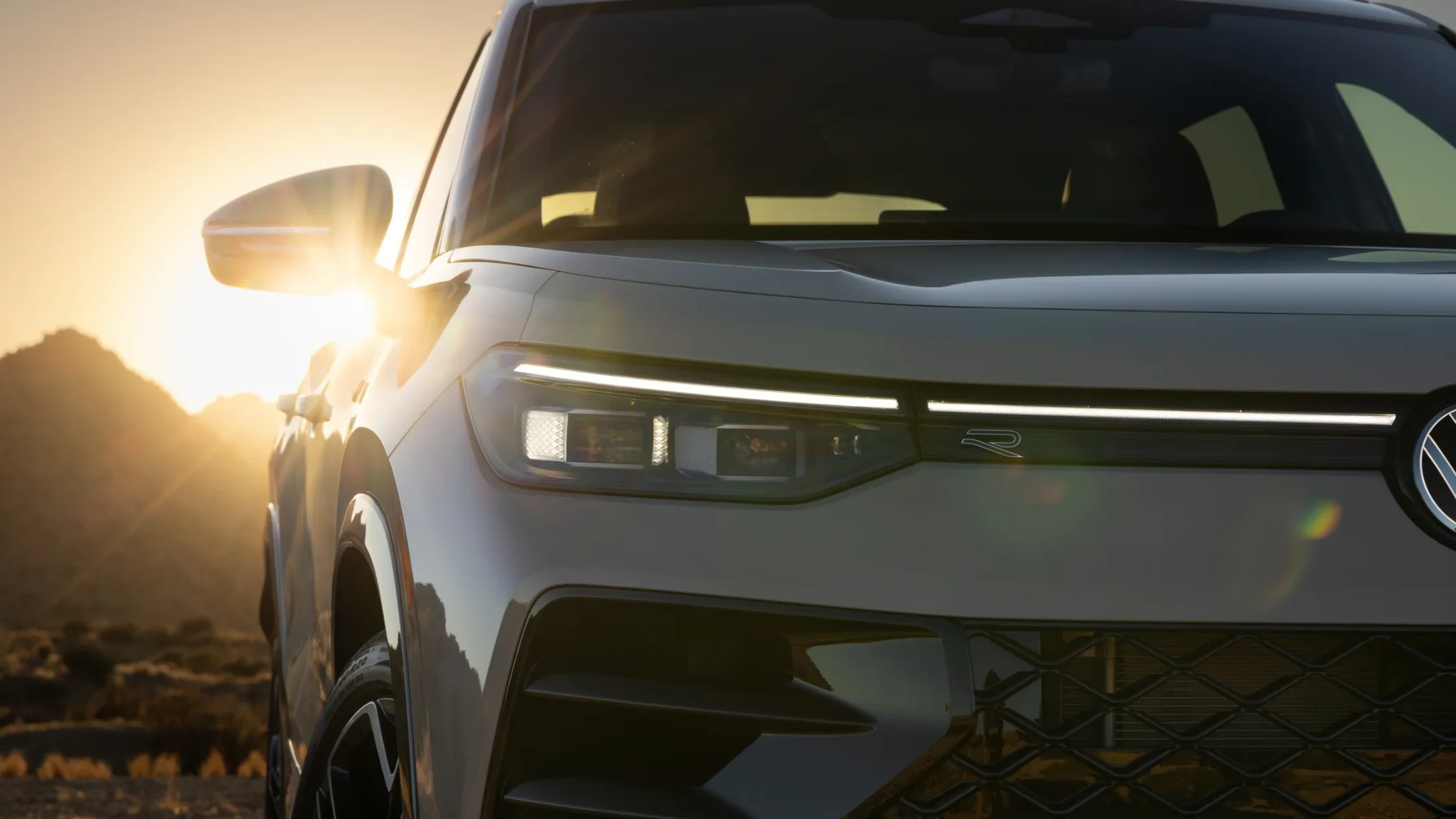 Close-up of the 2025 Volkswagen Tiguan's LED headlights and front grille with R-Line badge, illuminated by the setting sun.