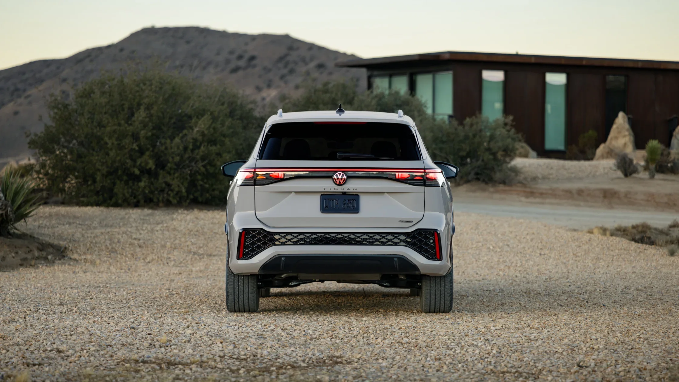 Rear view of the 2025 Volkswagen Tiguan highlighting its LED taillights, dual exhaust accents, and Tiguan badging with a modern home in the background.