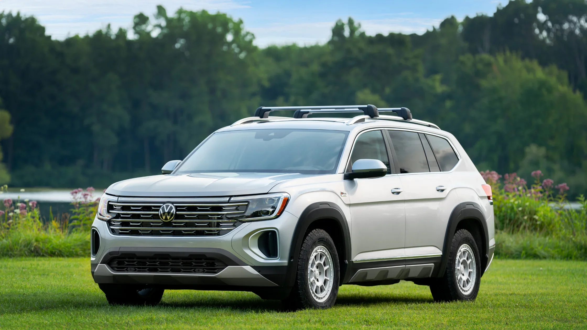 2025 Volkswagen Atlas SUV in silver parked on grass with roof rails and bold front grille design.