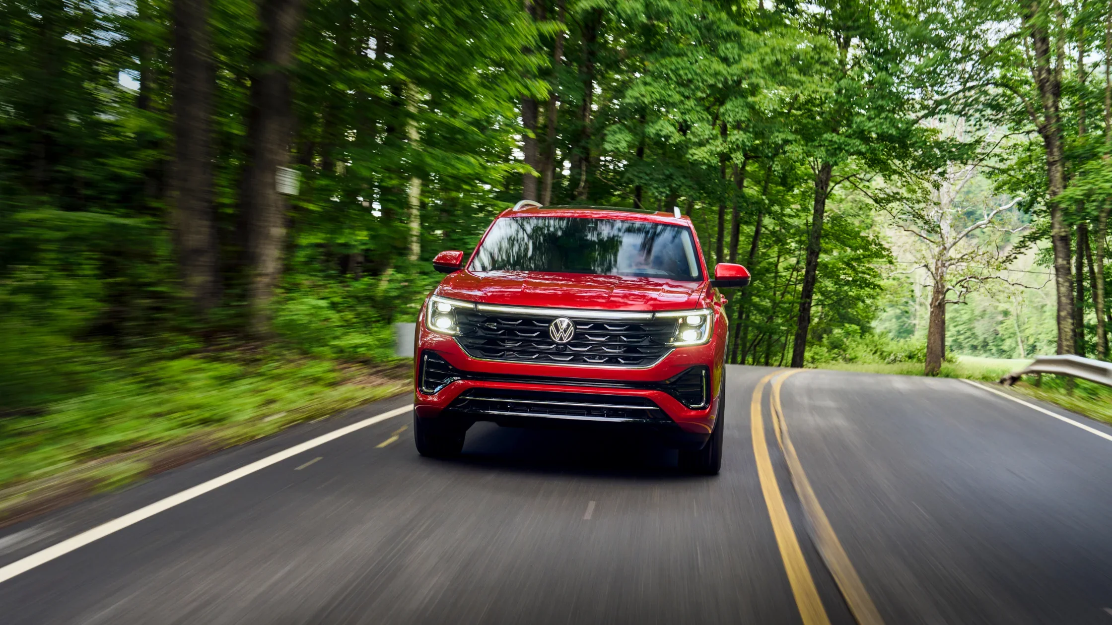 2026 Volkswagen Atlas in red driving through forest road with bold front grille.