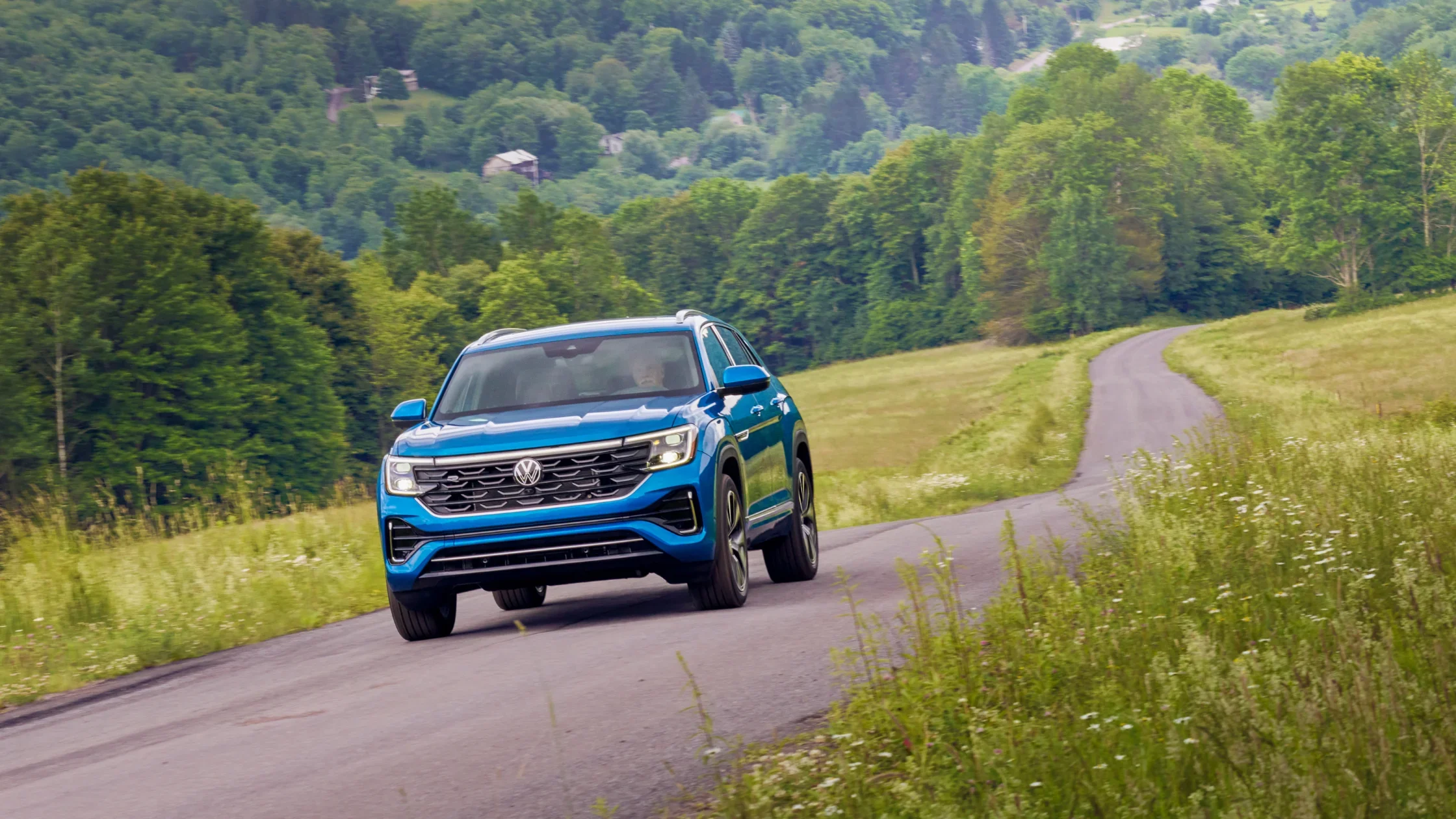 2026 Volkswagen Atlas Cross Sport in blue driving on winding countryside road.