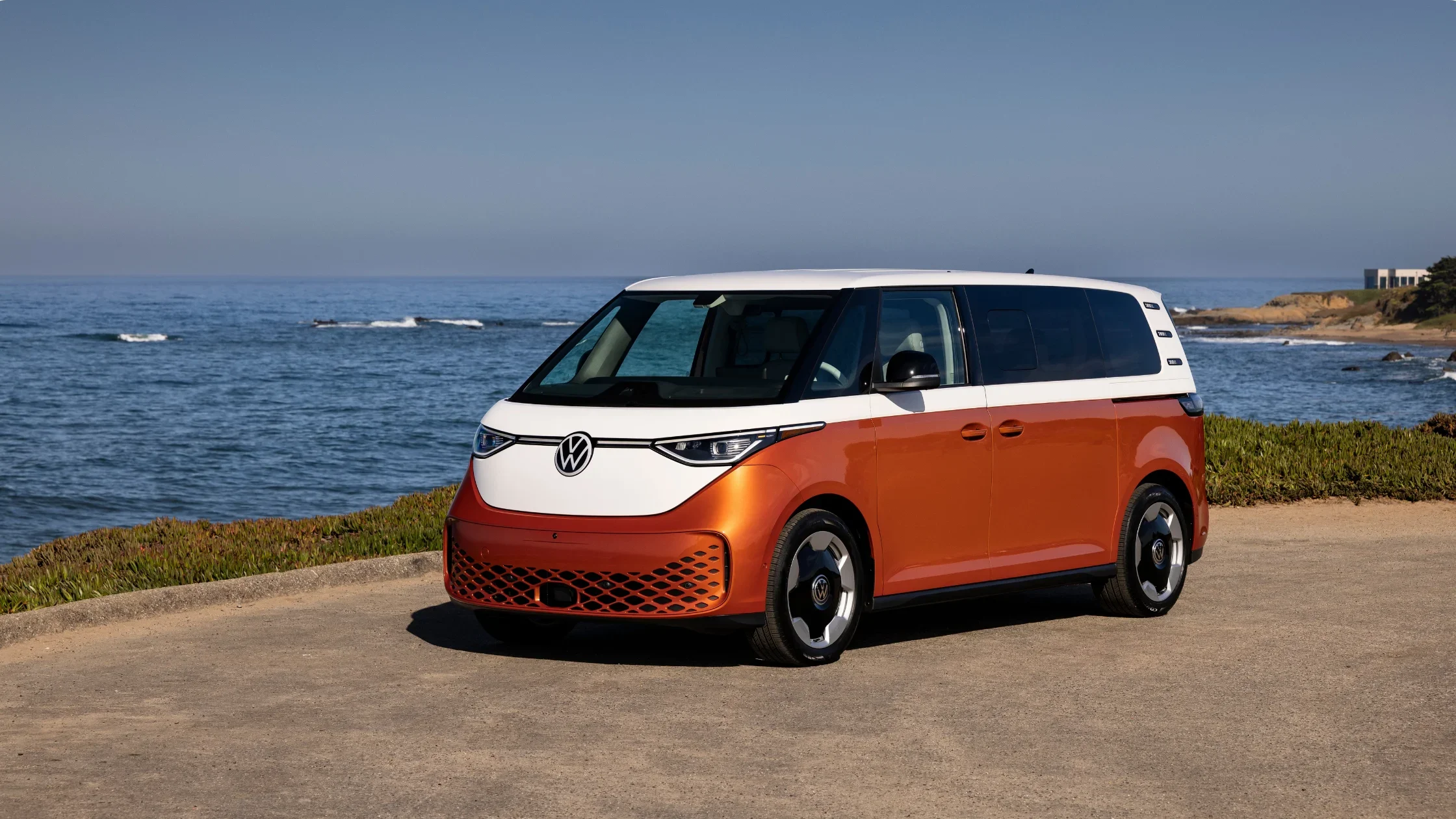 2025 Volkswagen ID. Buzz exterior side view in orange and white parked along coastal road.