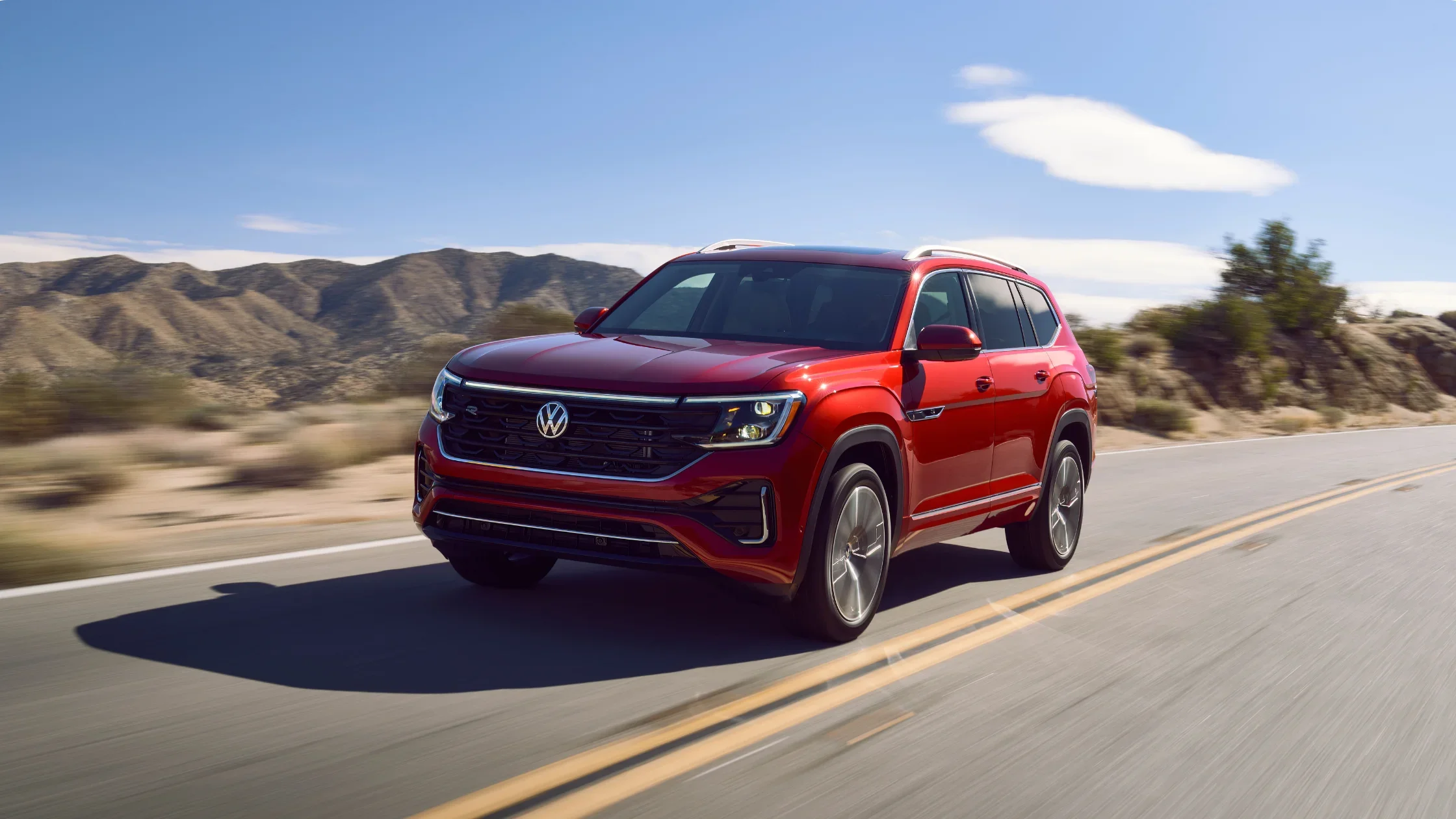 2026 Volkswagen Atlas exterior front view driving on highway in red finish.