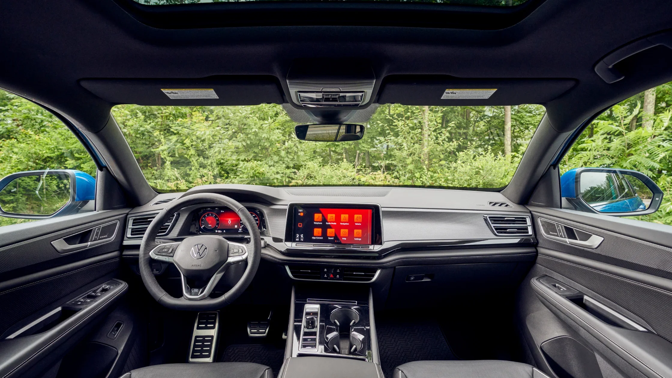 Front view of a blue 2025 Volkswagen Atlas Cross Sport driving through a forested road.