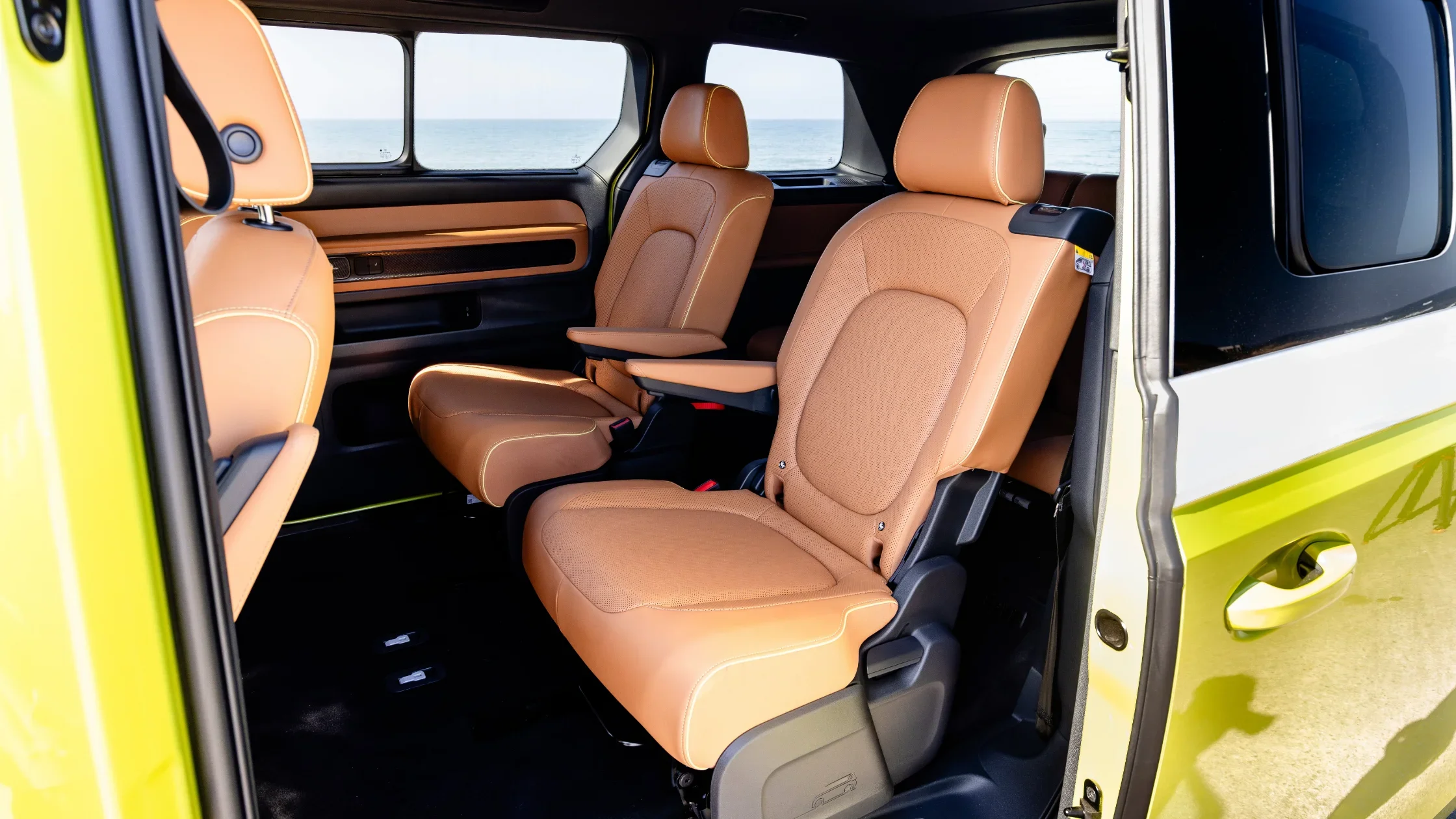Rear captain’s chairs in the 2025 Volkswagen ID. Buzz with tan upholstery and ocean background.