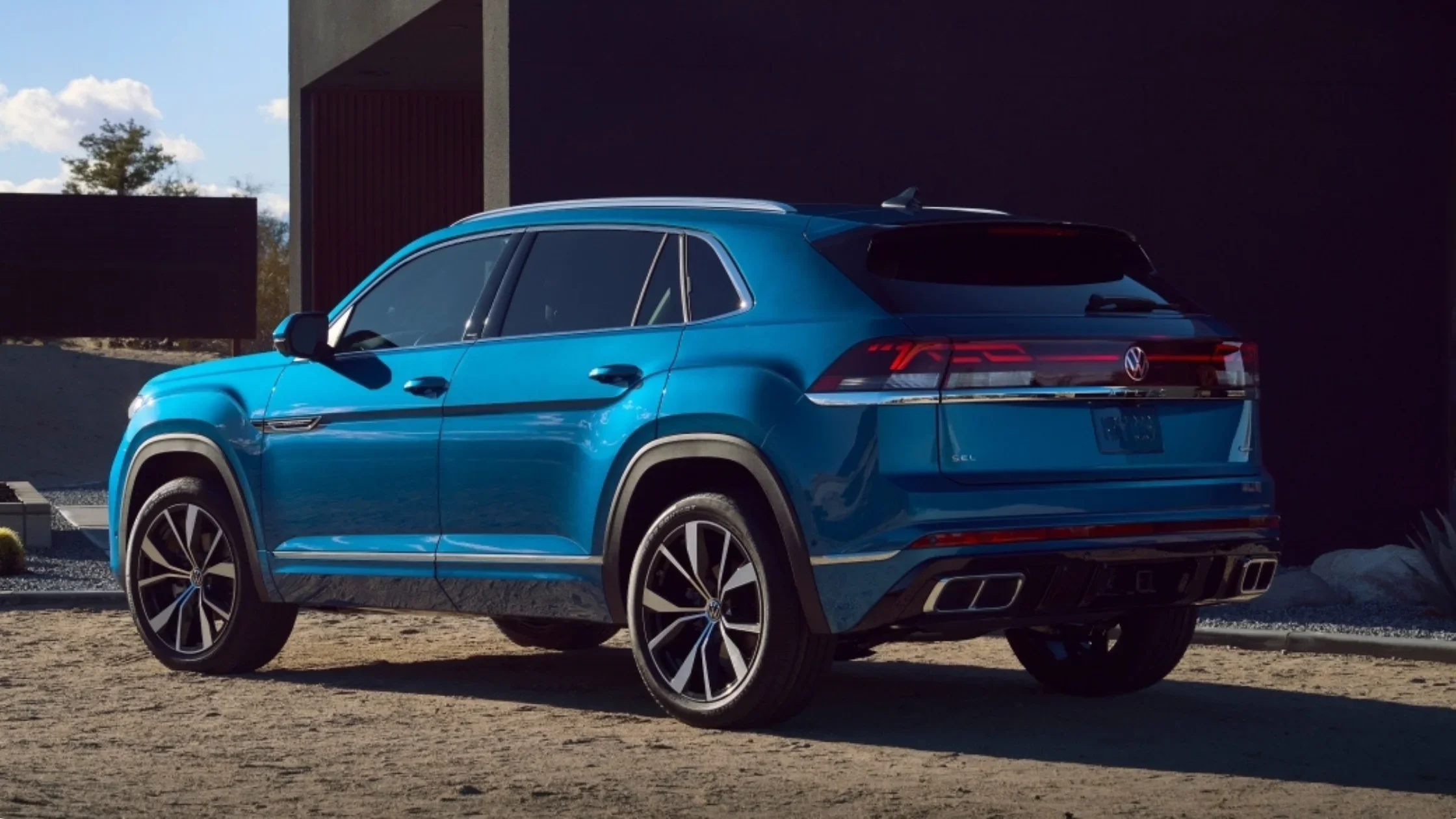 2026 Volkswagen Atlas Cross Sport blue SUV driving on a desert road in front three quarter view.