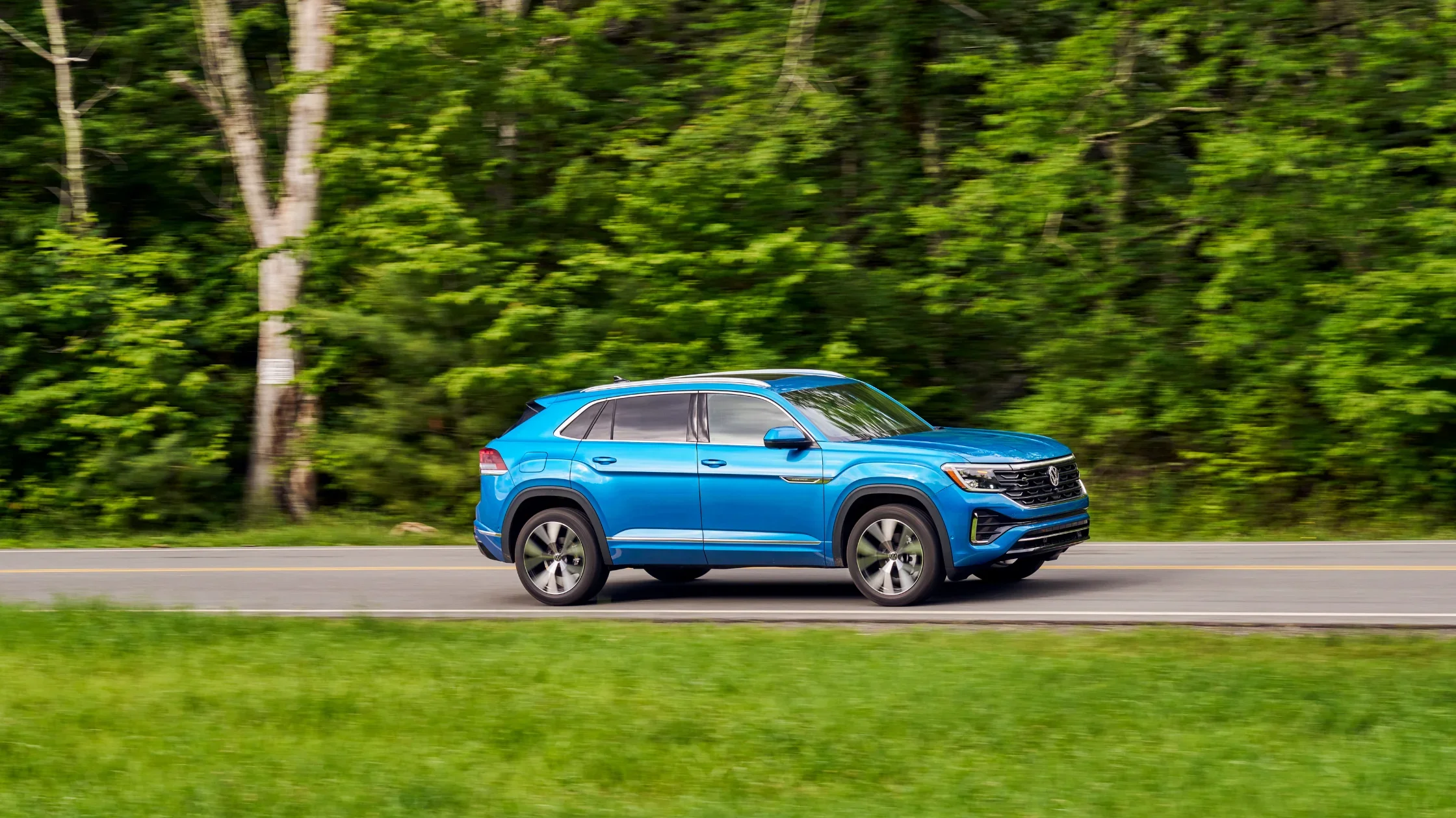 2026 Volkswagen Atlas Cross Sport blue exterior side profile driving on a scenic road.