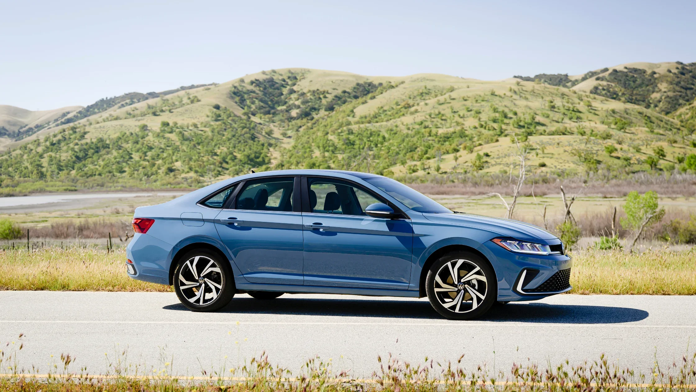 2026 Volkswagen Jetta blue exterior side profile parked roadside with mountain background.