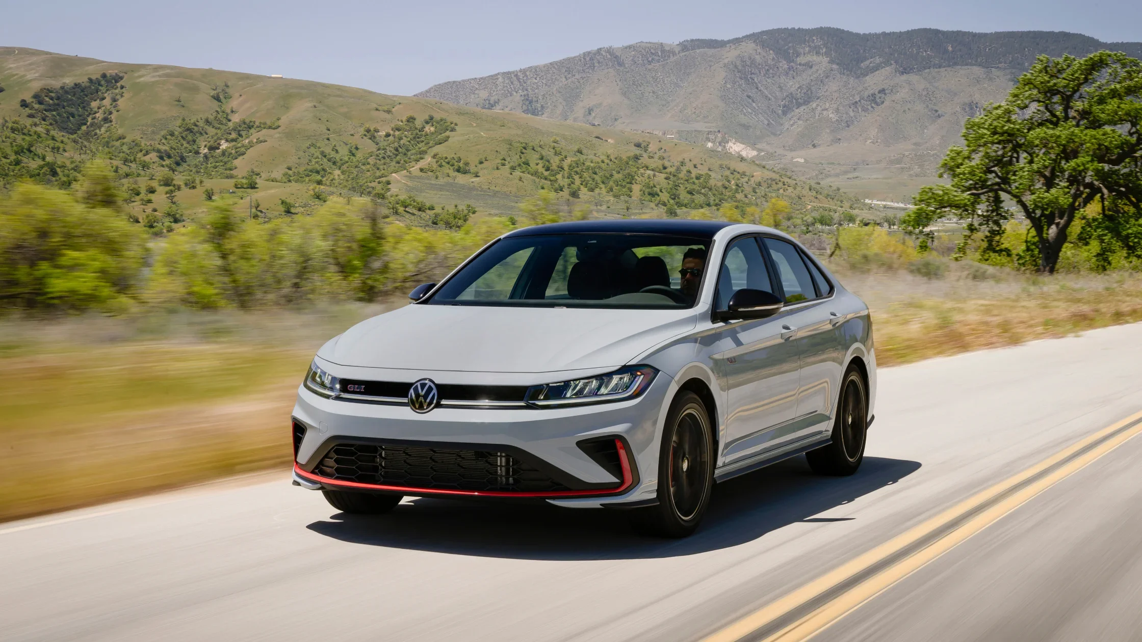 2026 Volkswagen Jetta GLI gray exterior front three quarter view driving through rolling hills